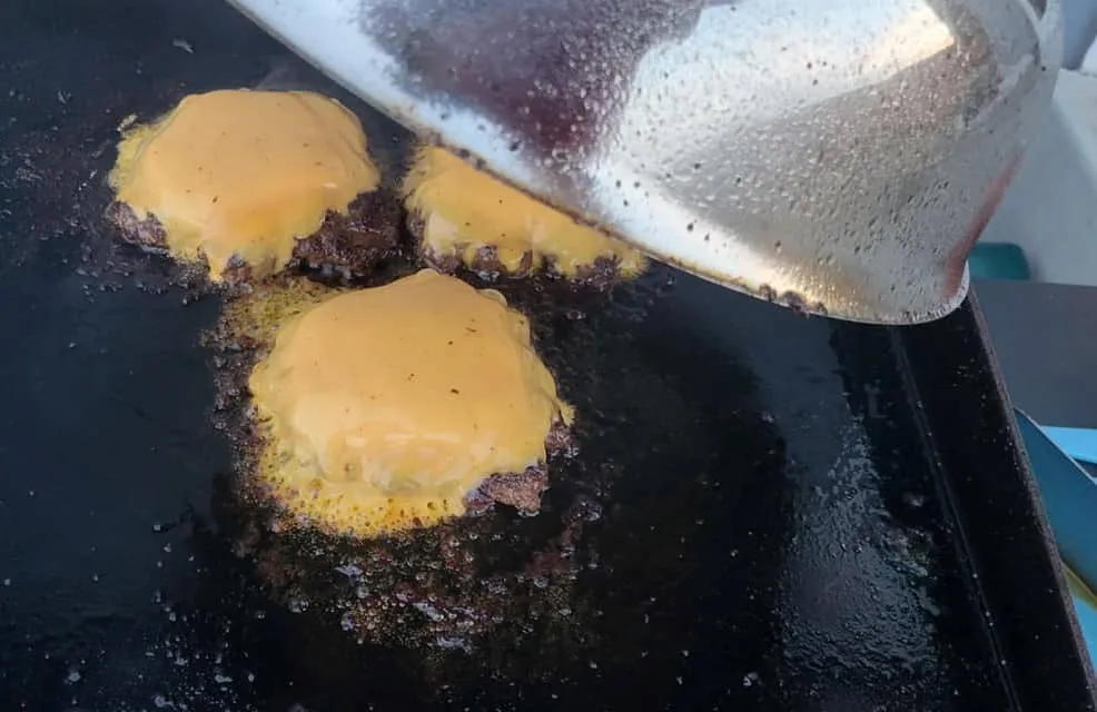 Basting dome over burgers on a Blackstone to melt cheese