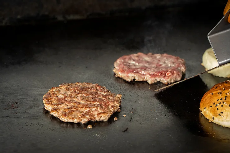 Stainless steel smash burger spatula pressing a burger on a flat-top griddle