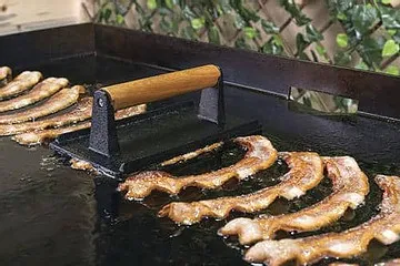 Bacon press on a Blackstone griddle keeping strips flat and in full contact with the surface