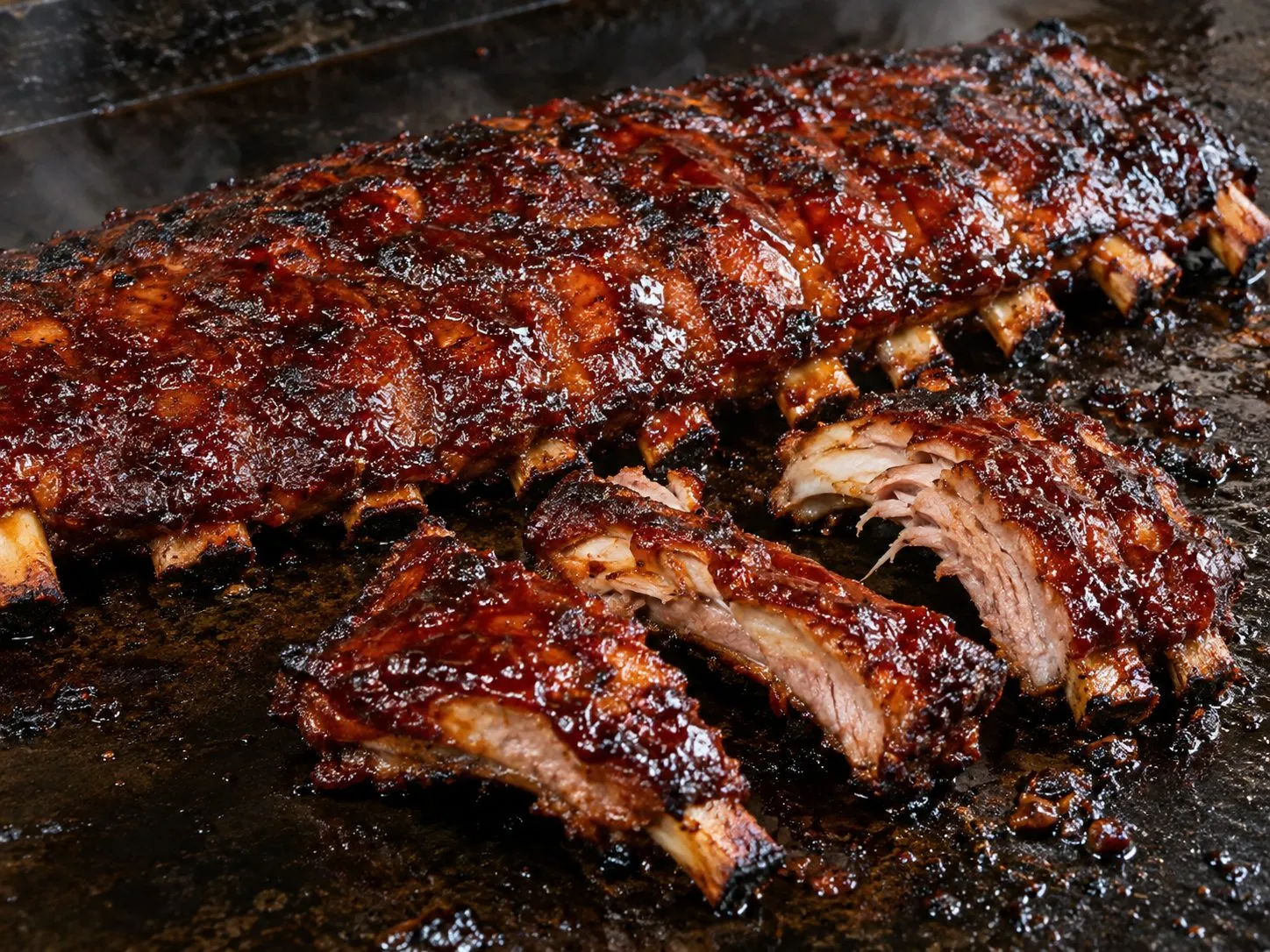 Glazed baby back ribs with a charred, caramelized bark, sliced between the bones, on a Blackstone griddle
