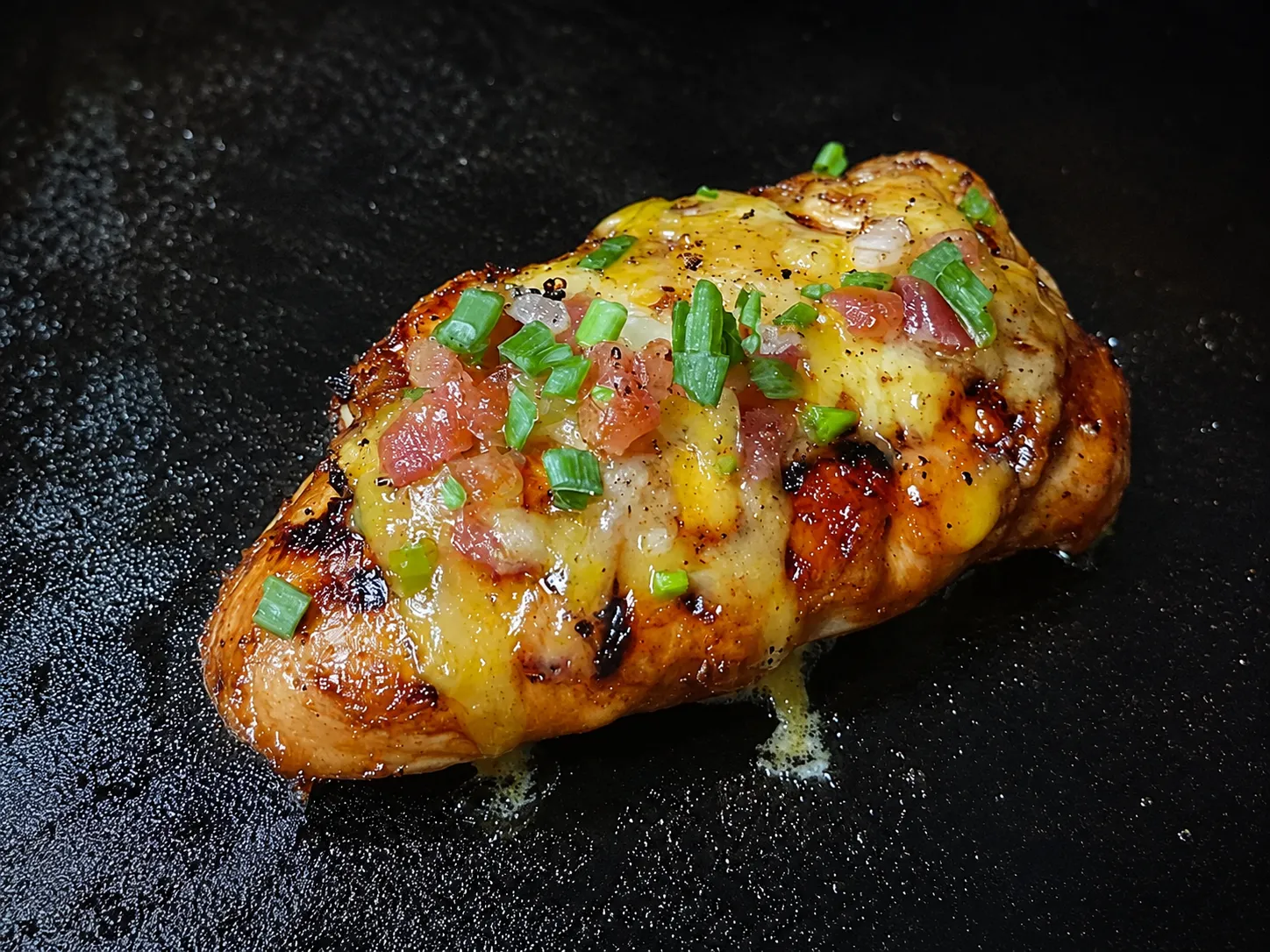 Loaded grilled chicken breast on a Blackstone griddle with melted cheese, tomatoes, and green onions