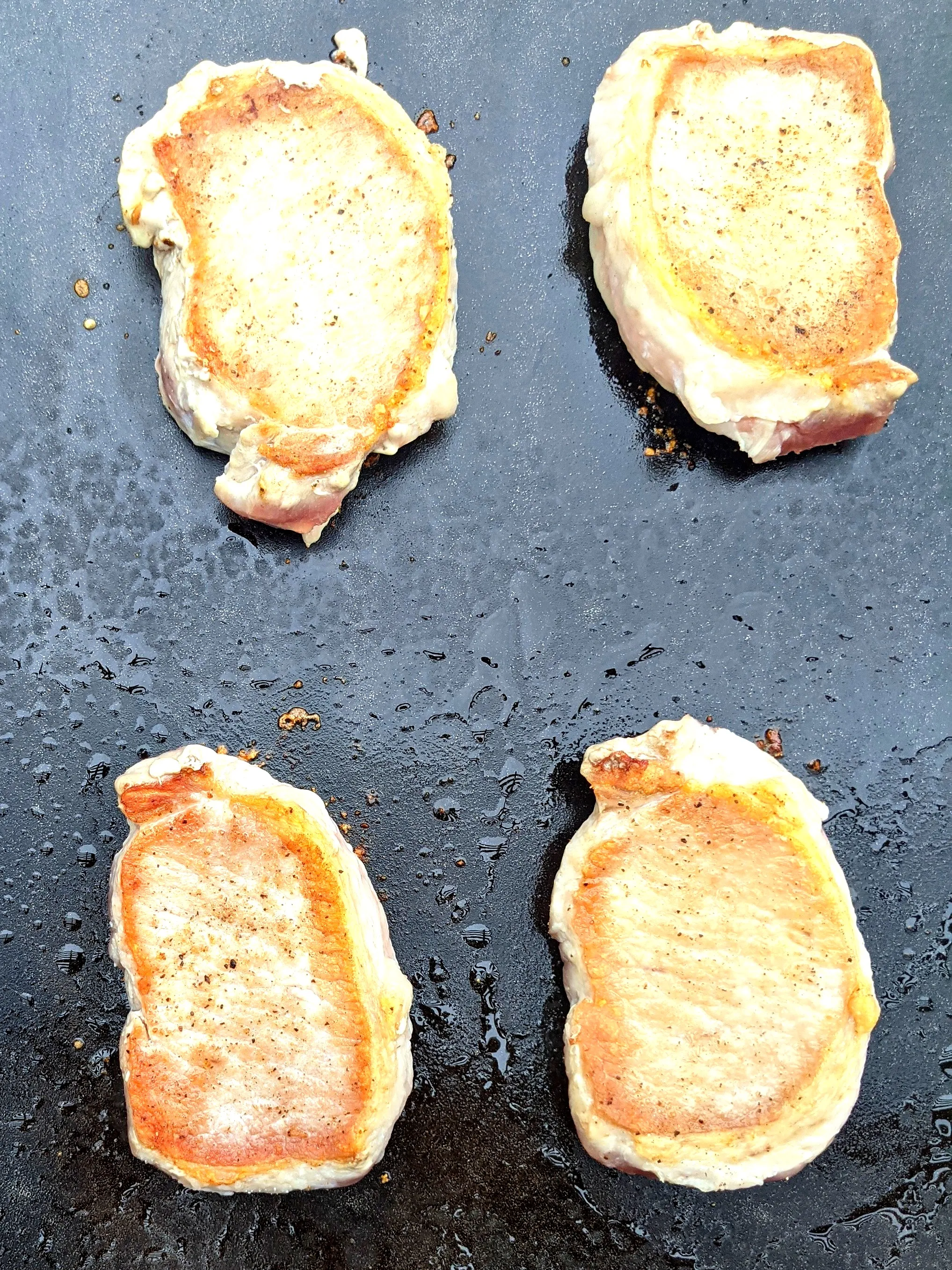 Blackstone pork chops searing on a flat-top griddle with golden crust